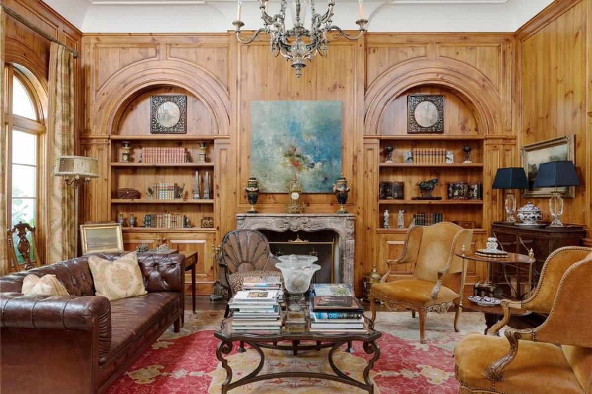 A living room with shelves, cabinets, a fireplace, chandelier, couch, chairs, and a center table.