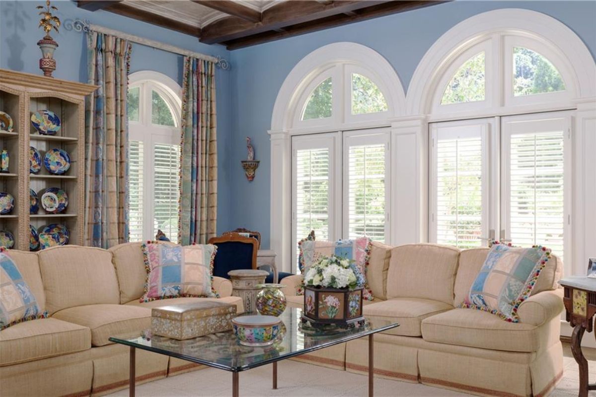 A living room with windows, couches with pillows, and a glass center table.