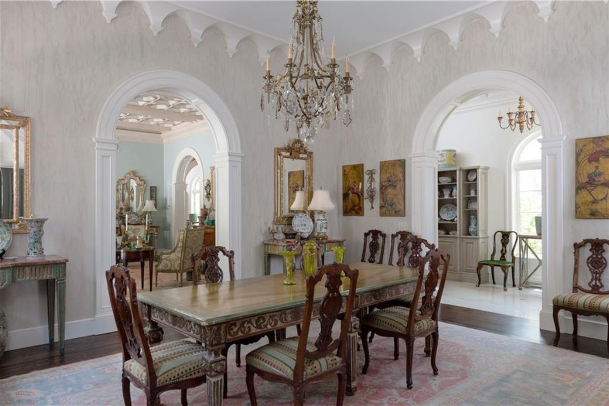 A dining room with a chandelier, ceiling molding, paintings, and a dining table surrounded by chairs.