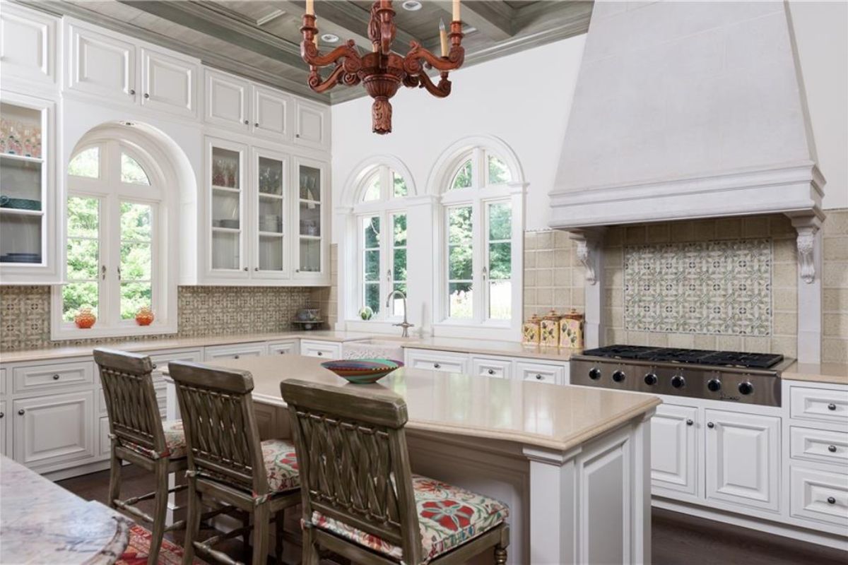 A kitchen with countertops, chairs, cabinets, windows, and a stove.