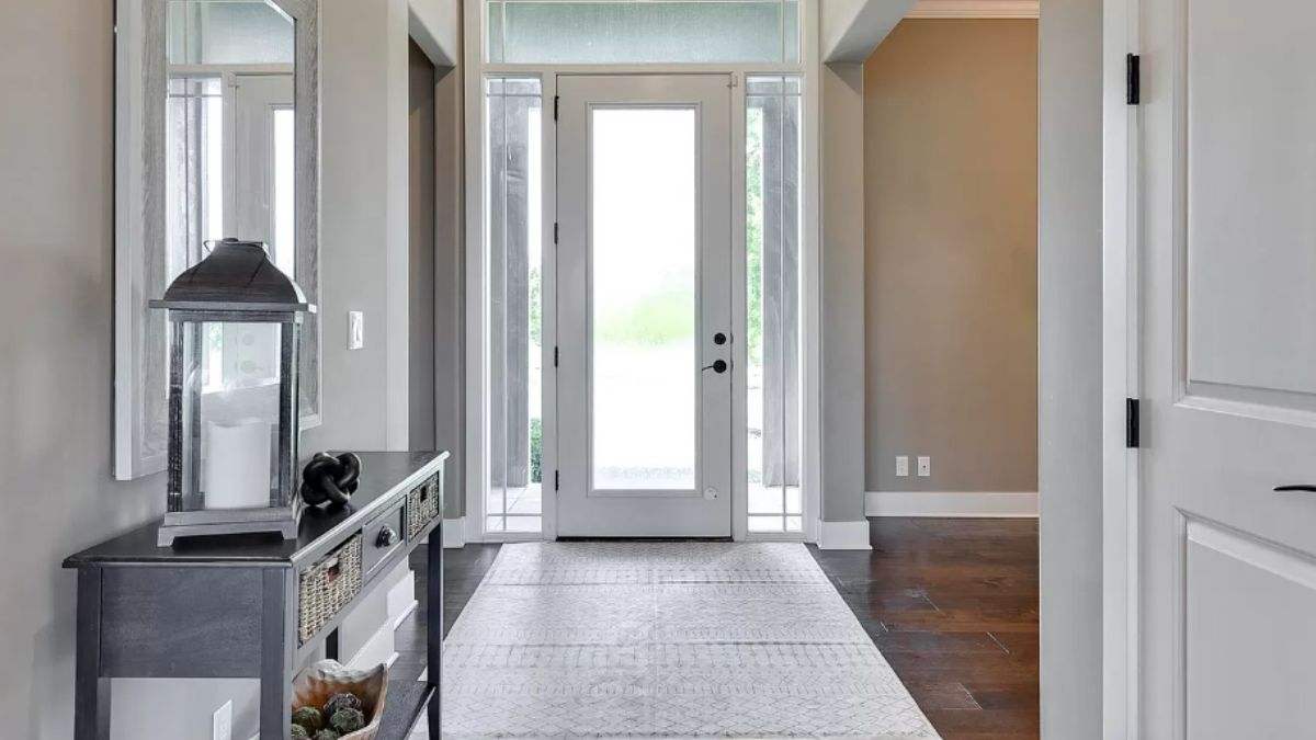 A foyer with a mirror, wooden floor, and rug.