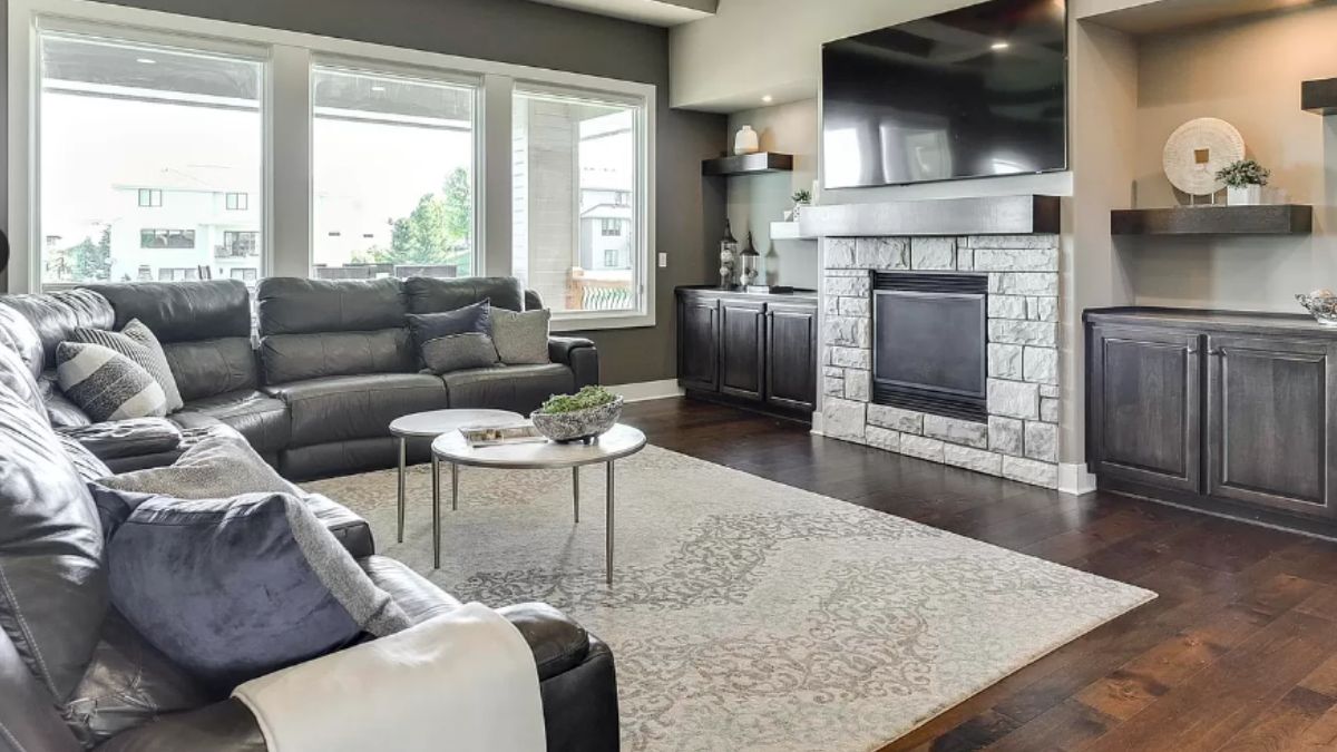 A living room with windows, TV, fireplace, cabinet, rug, couches with pillows, and a center table.