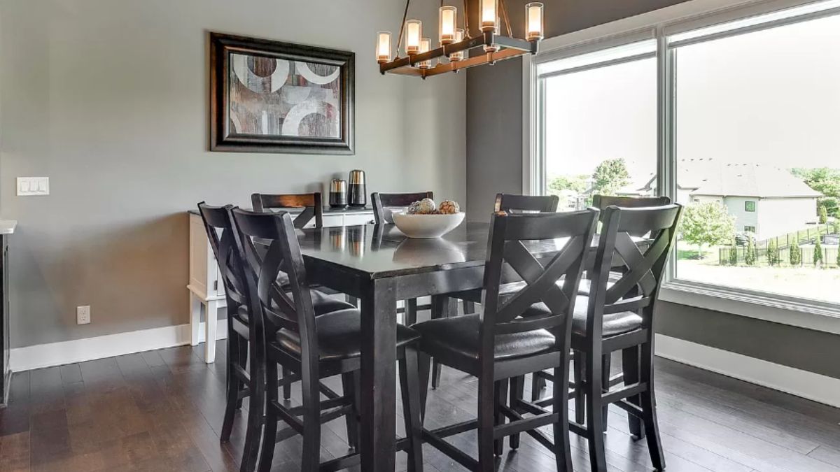 A dining area with a window, painting, and a table surrounded by chairs.