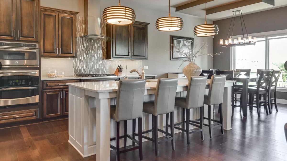 A kitchen with countertops, stools, cabinets, sink, and kitchen appliances.