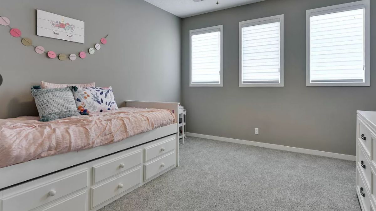 A bedroom with a bed, windows, and drawers.