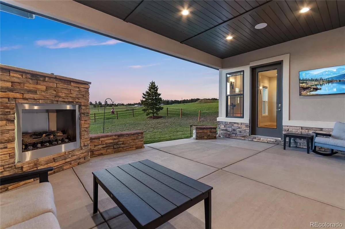 Covered porch with a stone fireplace and wood-paneled ceiling.