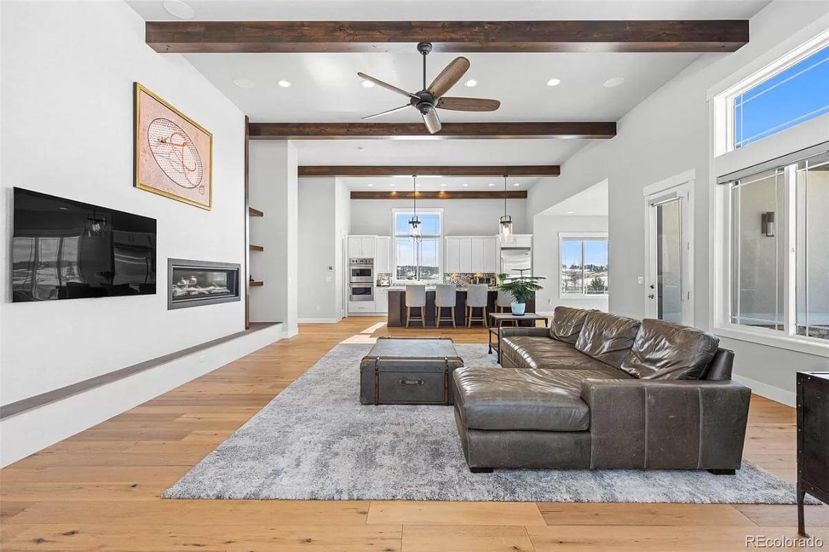 The living room includes a wall-mounted TV, a fireplace, and a beamed ceiling.