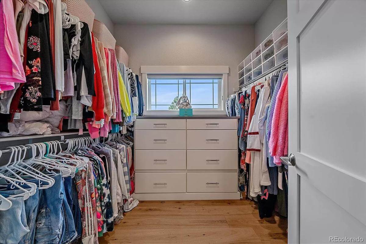 Primary walk-in closet with ample storage and a small window fixed above the dresser.