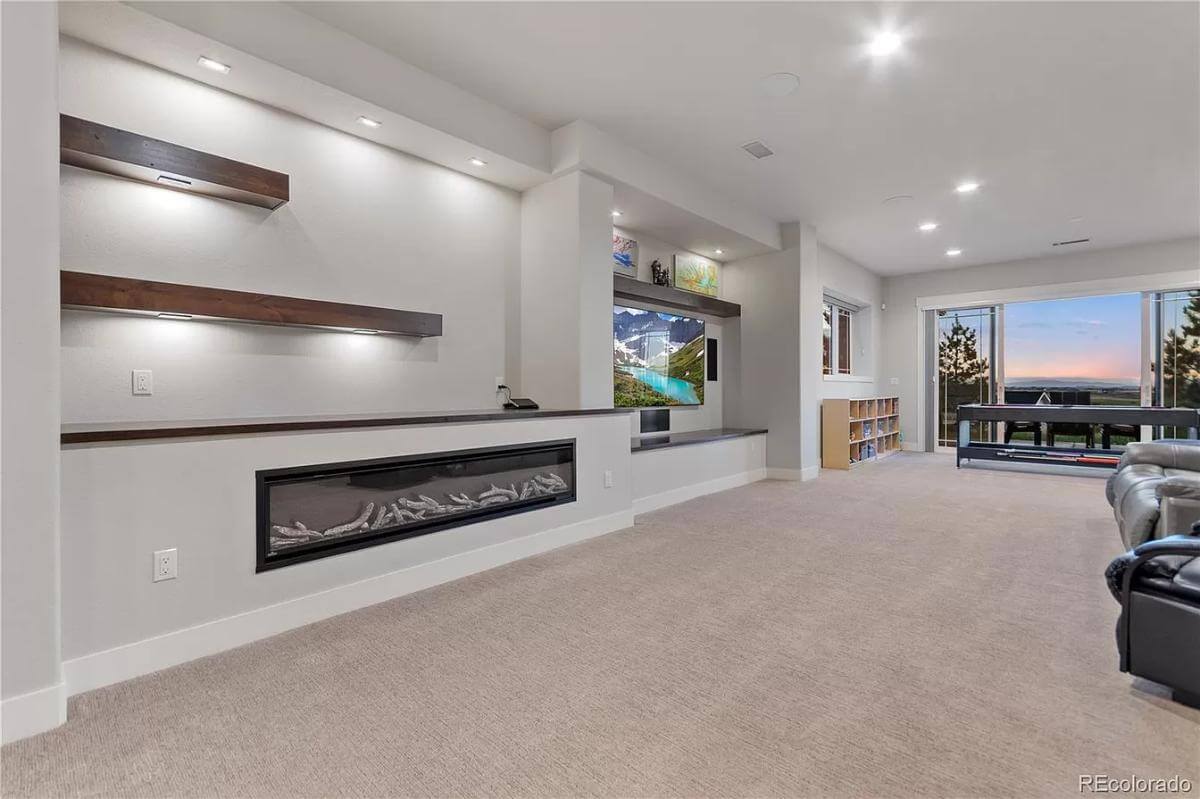 Basement with a linear fireplace, a wall-mounted TV, leather sofas, and outdoor access via glass sliders.