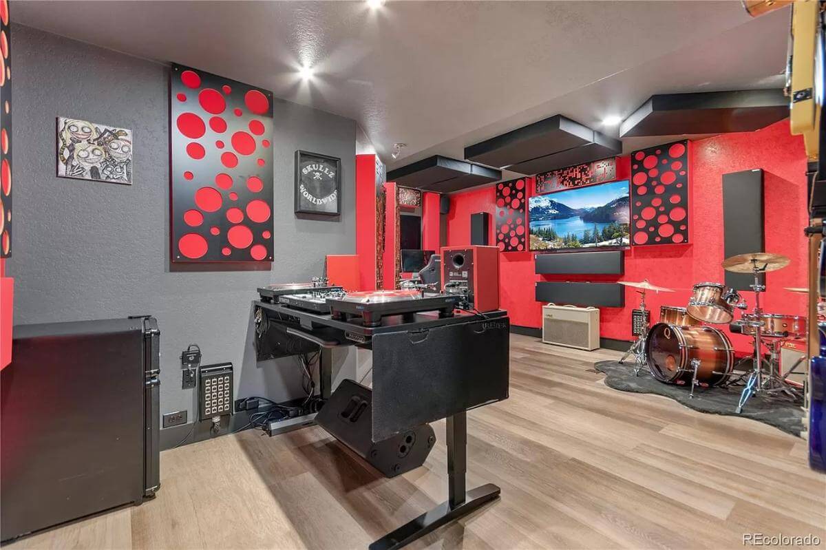 Music room with hardwood flooring and red and black walls adorned by posters and dotted artworks.