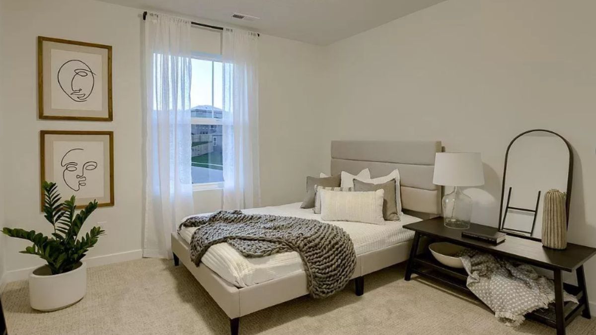 A bedroom with a potted plant, window, mirror, and side table.