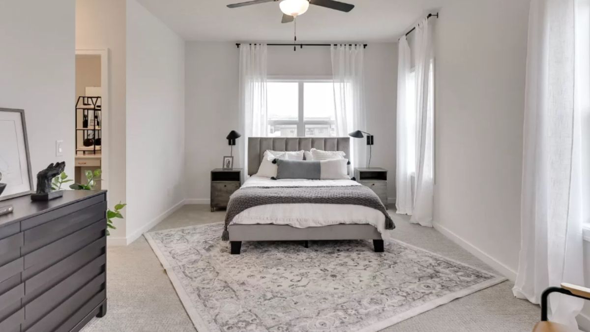 A bedroom with a bed, cabinets, mirror, windows, and a ceiling fan.