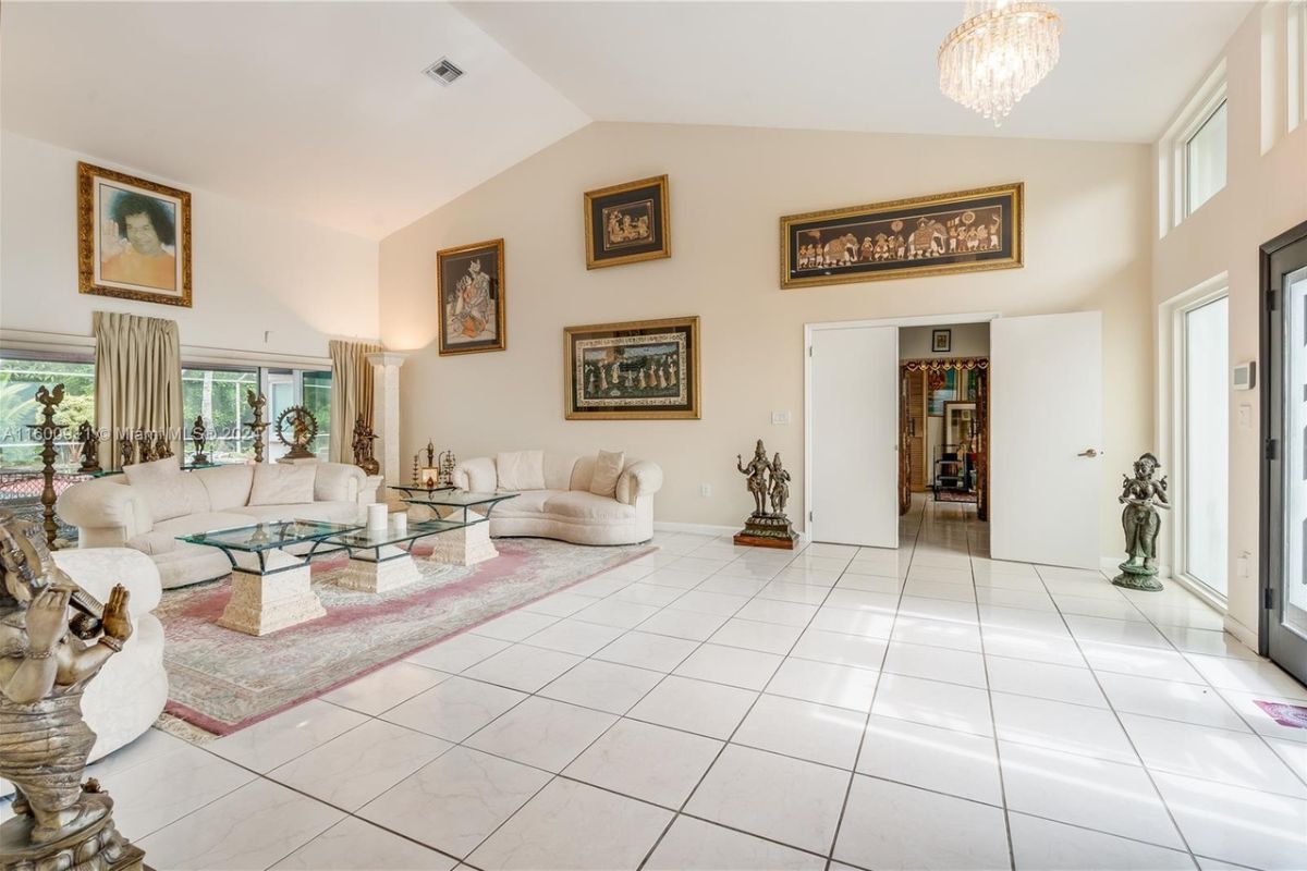 A living room with a vaulted ceiling, paintings, a rug, statues, white couches, and a glass center table.