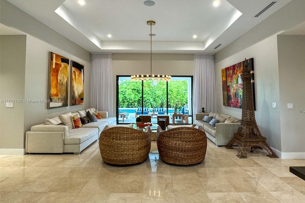 A living room with a chandelier, paintings, white couches, chairs, and a center table.