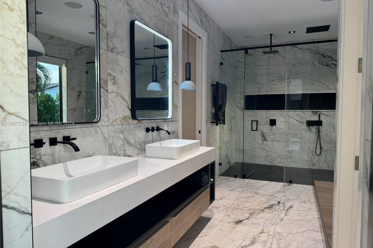 A bathroom with dual vanity, mirrors, and a shower room.