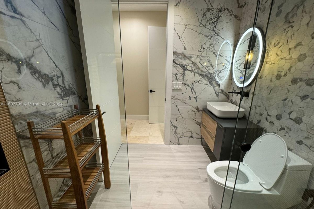 A bathroom with marble walls, vanity, mirror, and toilet.