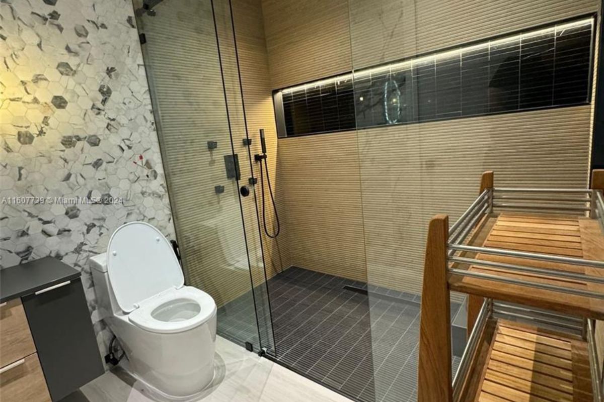 A bathroom with marble walls, shower room, and toilet.