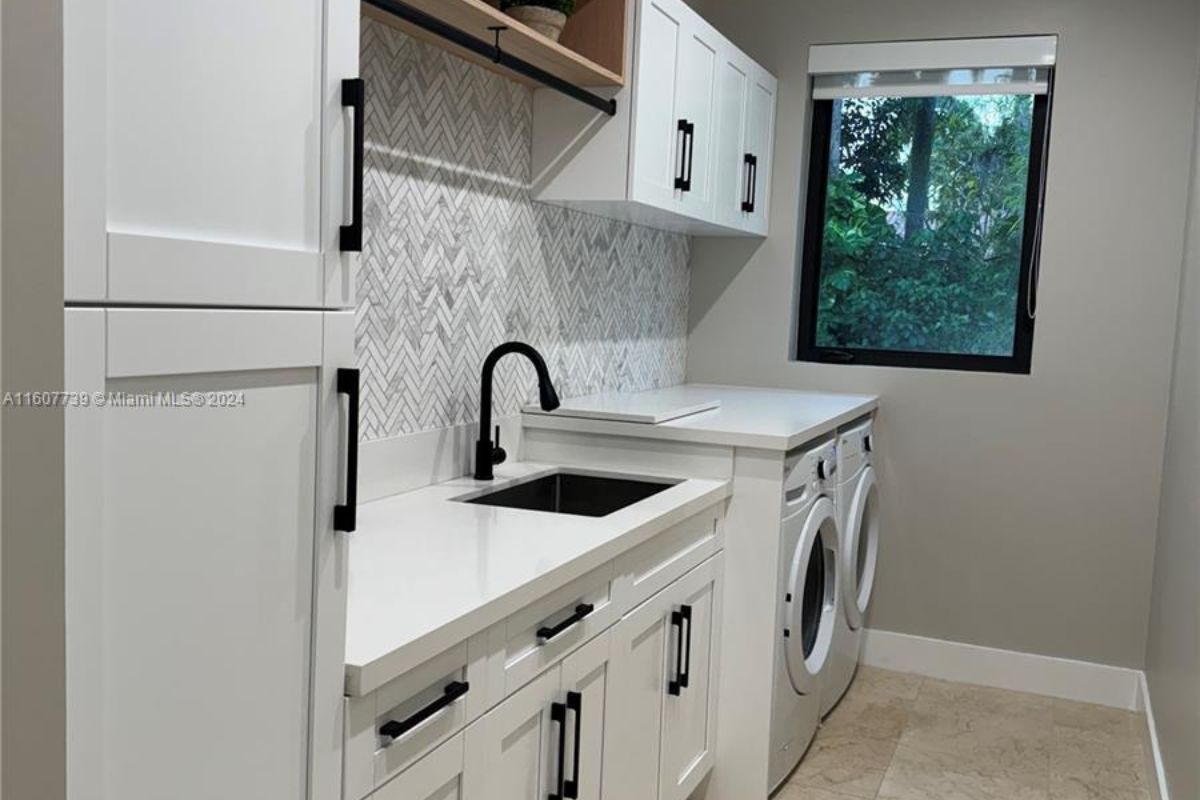 A laundry room with countertop, sink, cabinets, and washing machines.