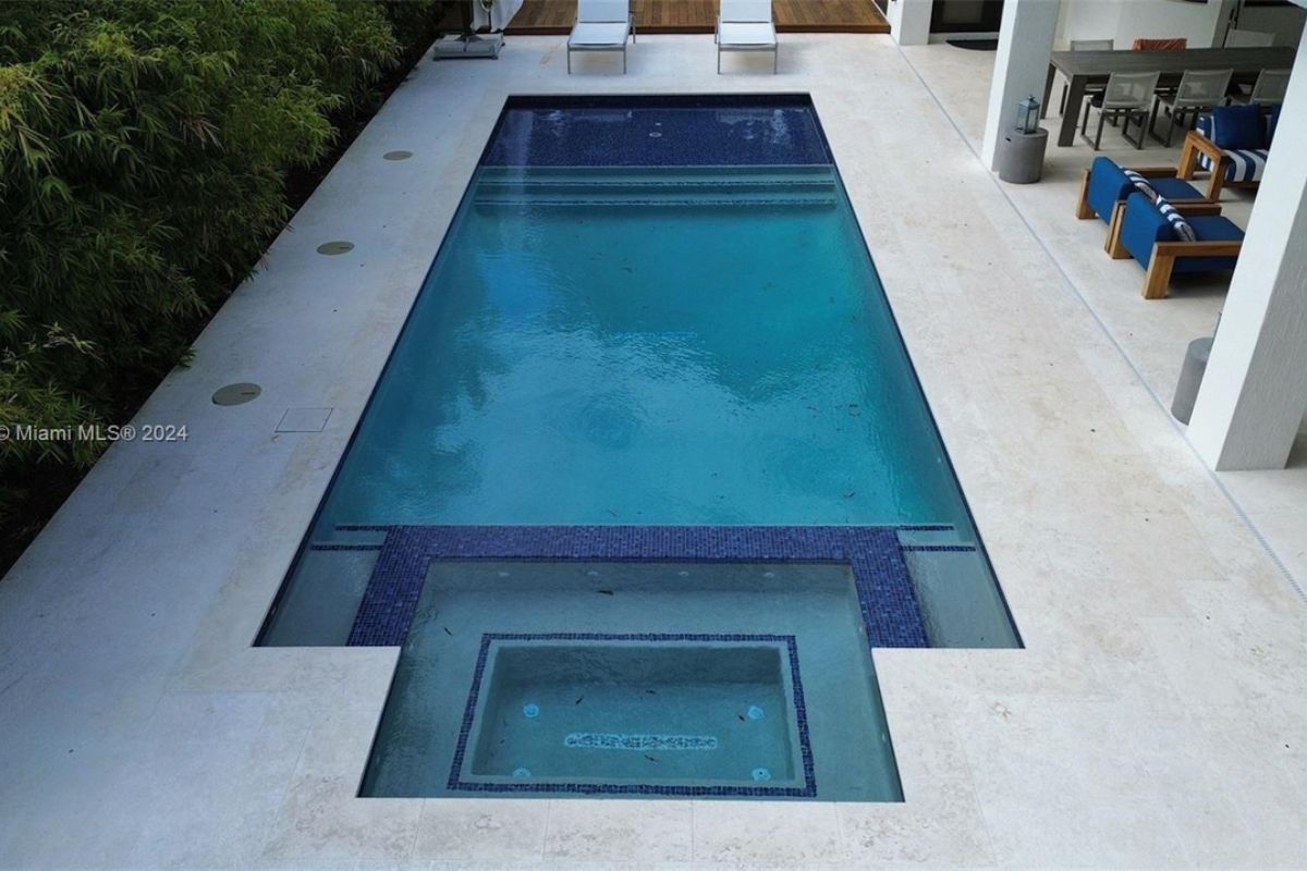 A swimming pool with a jacuzzi, chairs, and plants on the poolside.