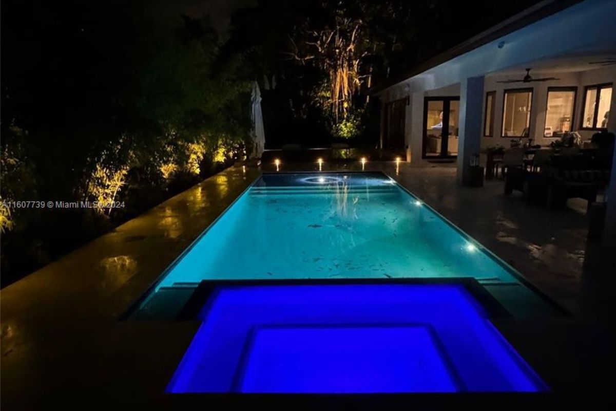 A swimming pool with a jacuzzi, chairs, and plants on the poolside.