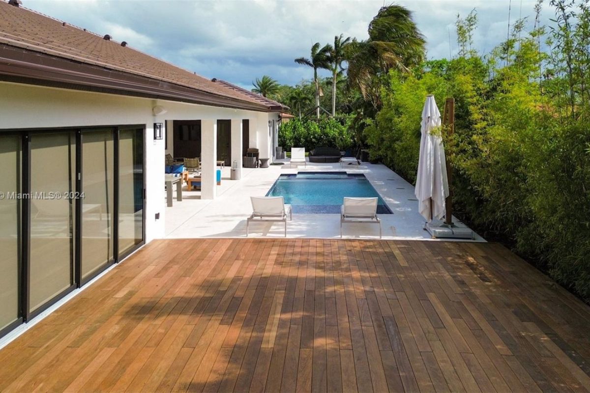 A swimming pool with a jacuzzi, chairs, and plants on the poolside.