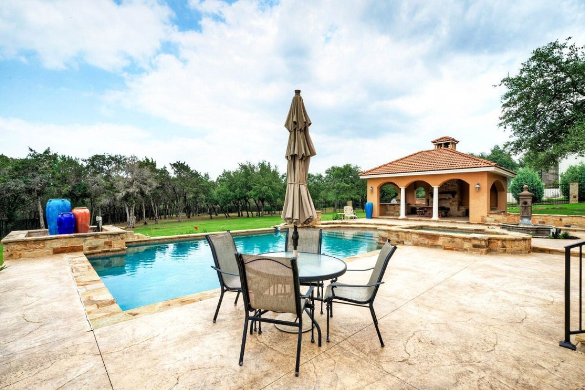 A swimming pool with a Jacuzzi, and a table with an umbrella and chairs on the poolside.