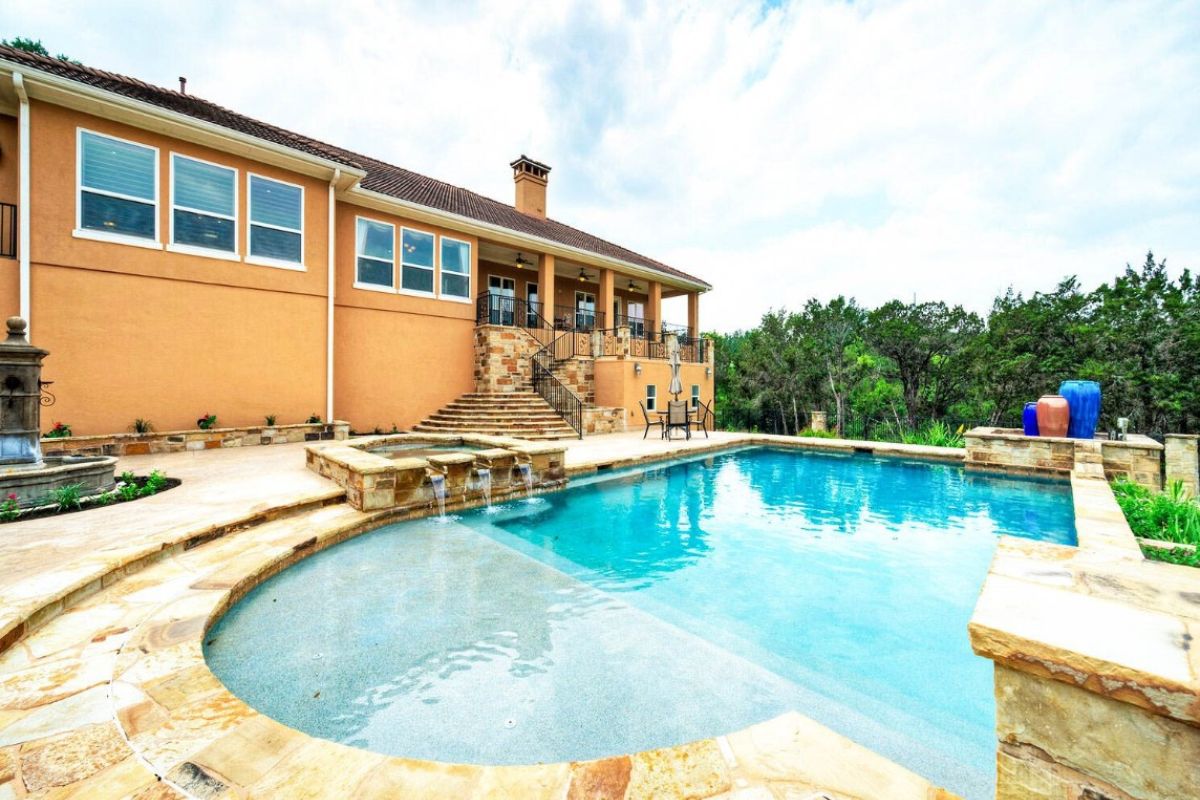 A swimming pool with a Jacuzzi, and a table with an umbrella and chairs on the poolside.