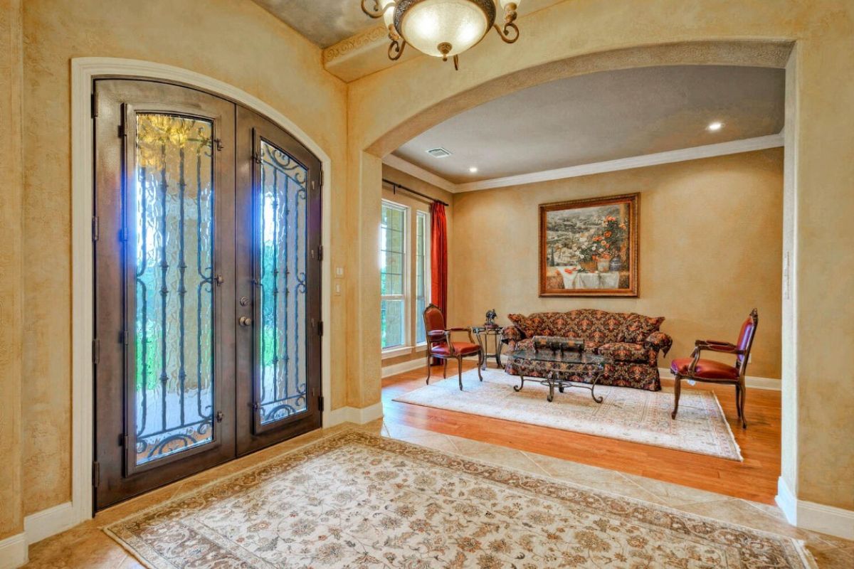 A foyer with a rug, chandelier, painting, chairs, couch, and glass center table.