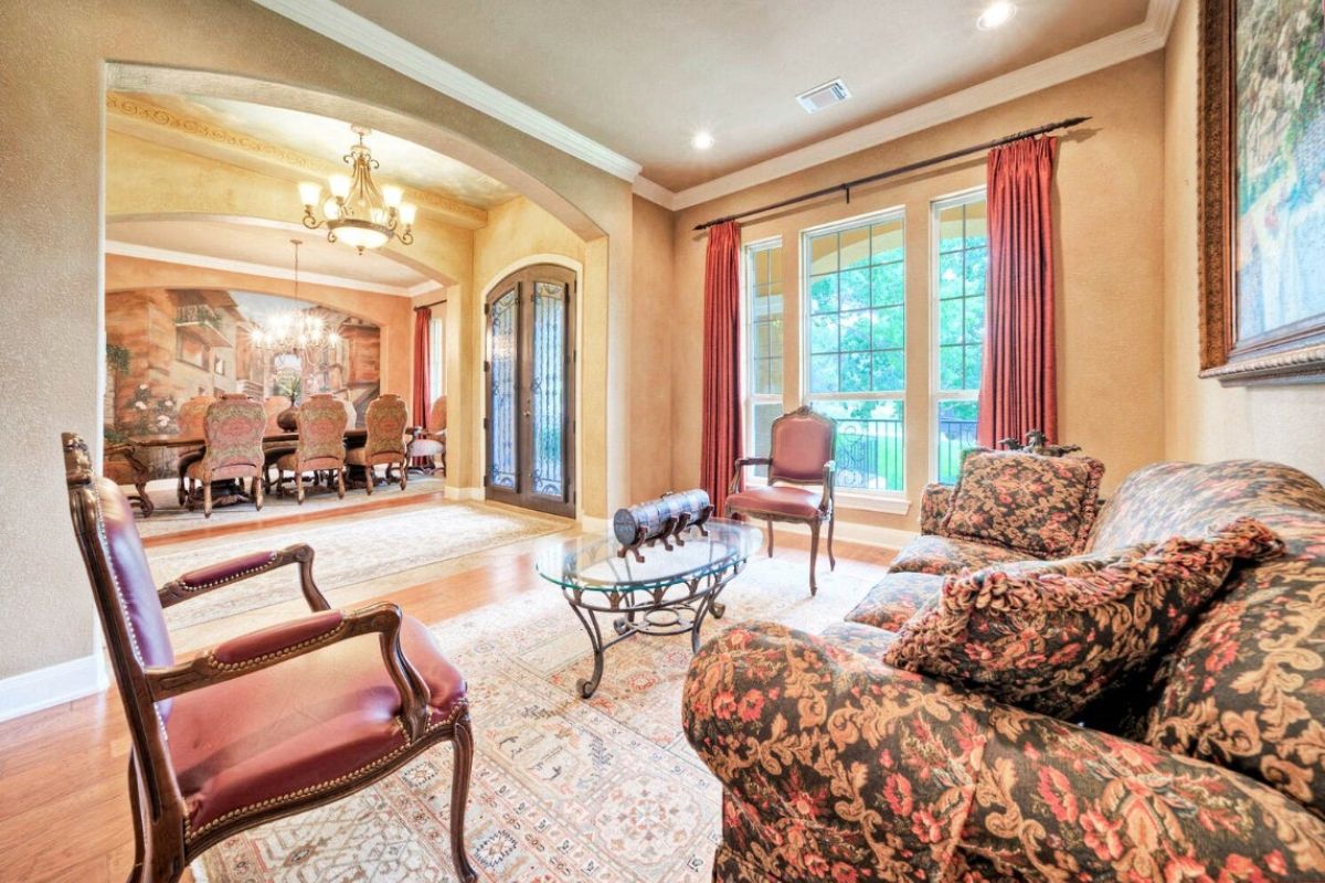 A living room with a painting, chairs, couch, and a glass center table.