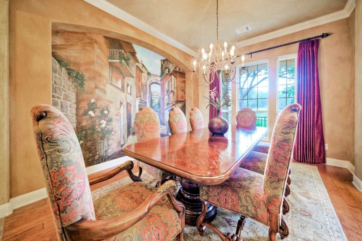 A dining room with painted walls, a chandelier, windows, and a dining table surrounded by chairs.