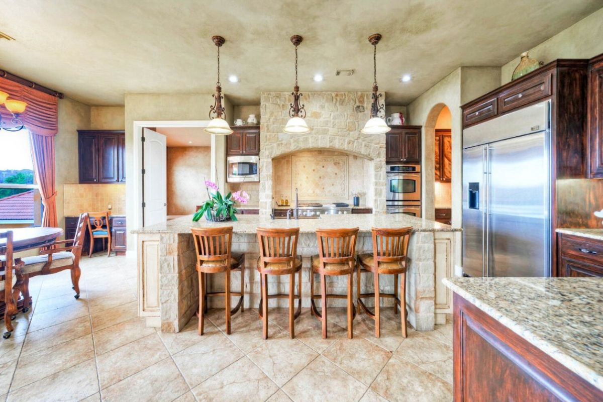 A kitchen with countertops, stools, sink, and kitchen appliances.