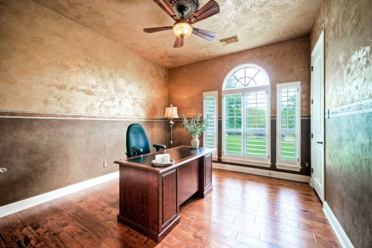 A home office with a window, wooden floor, ceiling fan, desk, and chair.