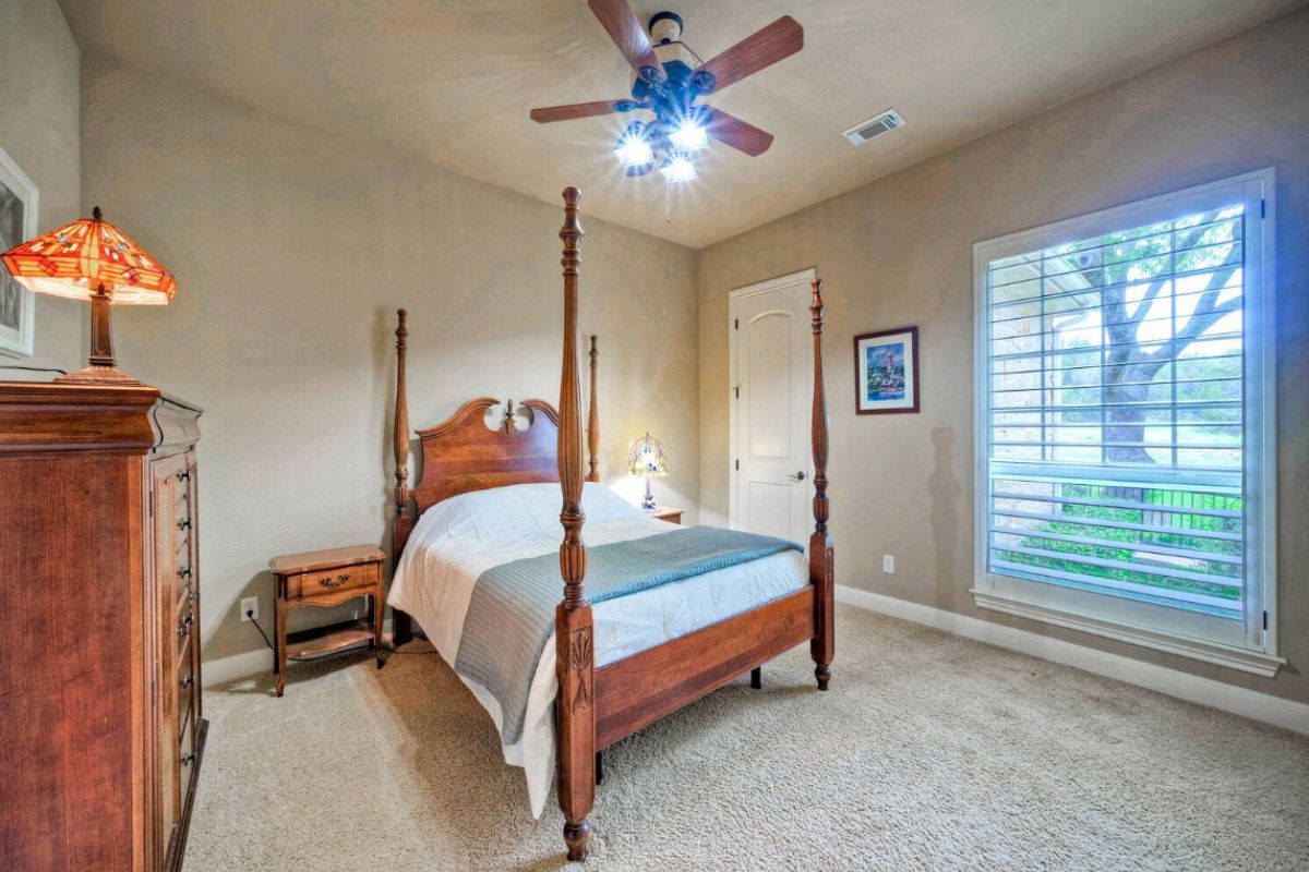 A bedroom with a bed, ceiling fan, cabinet, nightstand, and window.