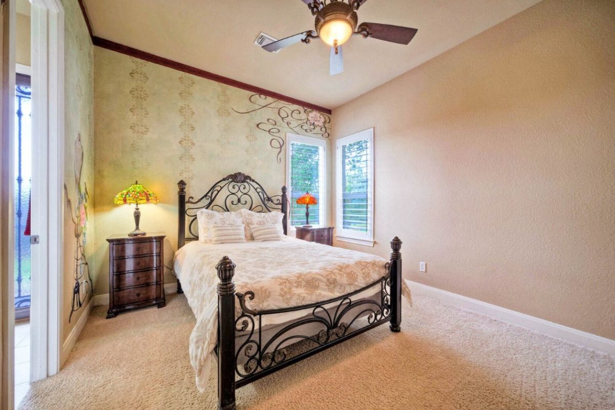 A bedroom with a bed, nightstand, windows, and a ceiling fan.