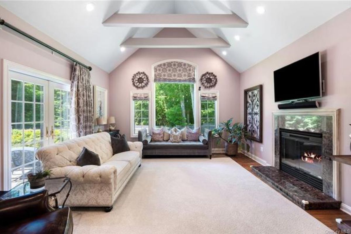 A living room with windows, a vaulted ceiling, a TV, a fireplace, and couches with pillows.