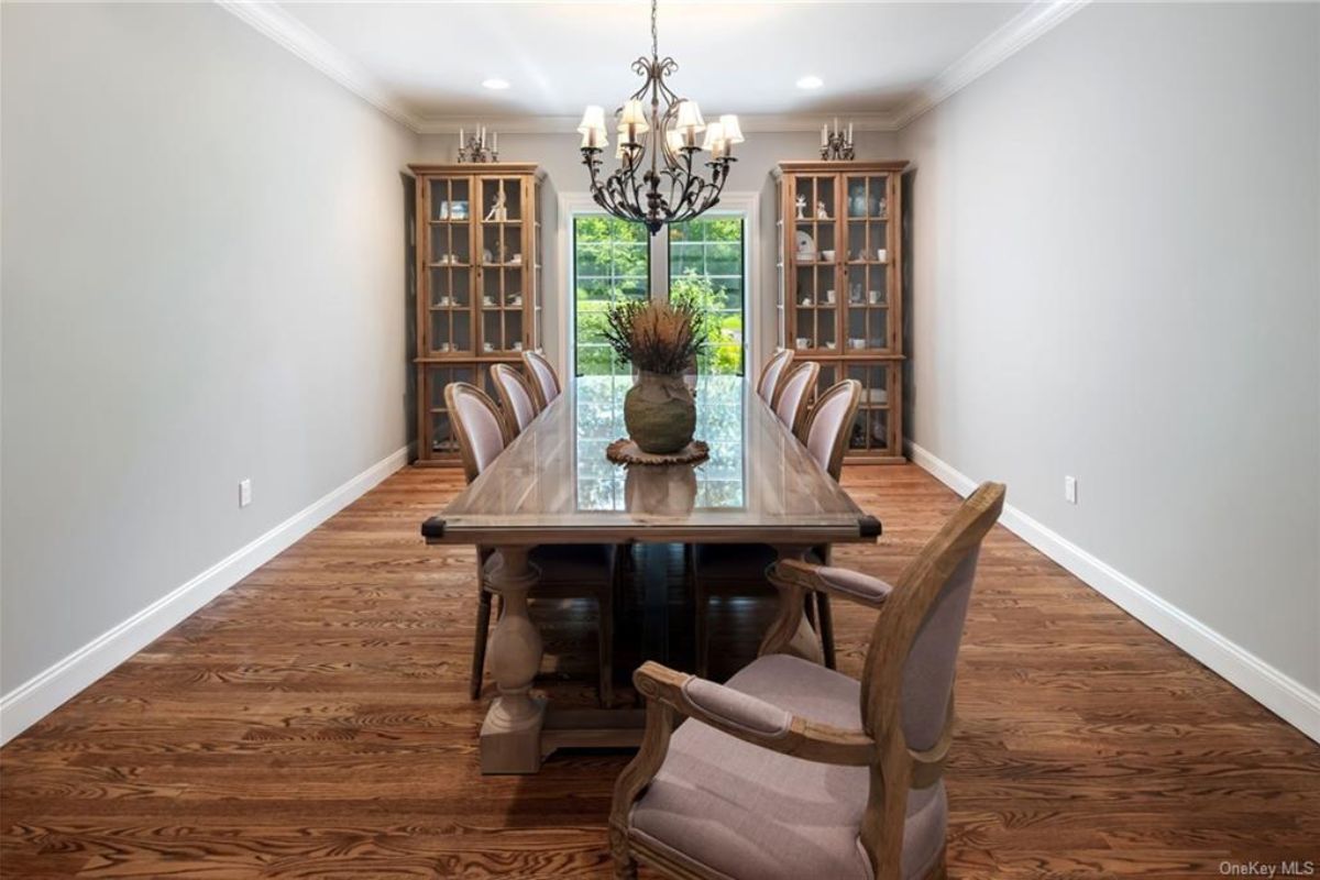 A dining room with cabinets, a chandelier, wooden floors, and a dining table surrounded by chairs.