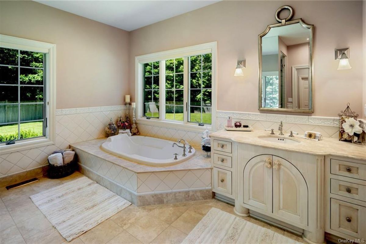 A bathroom with a vanity, cabinets, mirror, windows, and a bathtub.