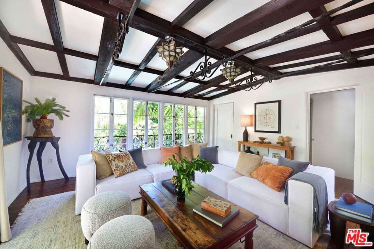 A living room with windows, an exposed beam ceiling, a white couch, and a center table.