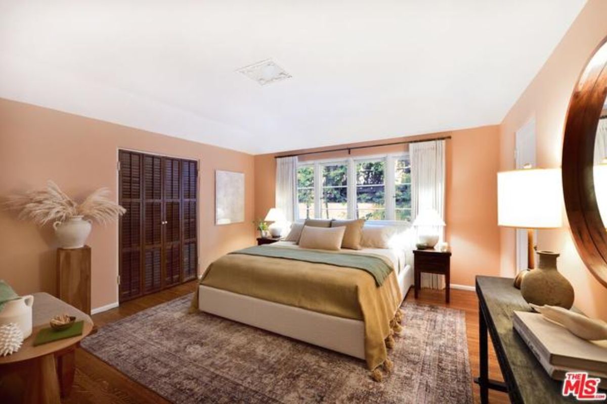 A bedroom with a bed, window, desk, vases, and a nightstand.