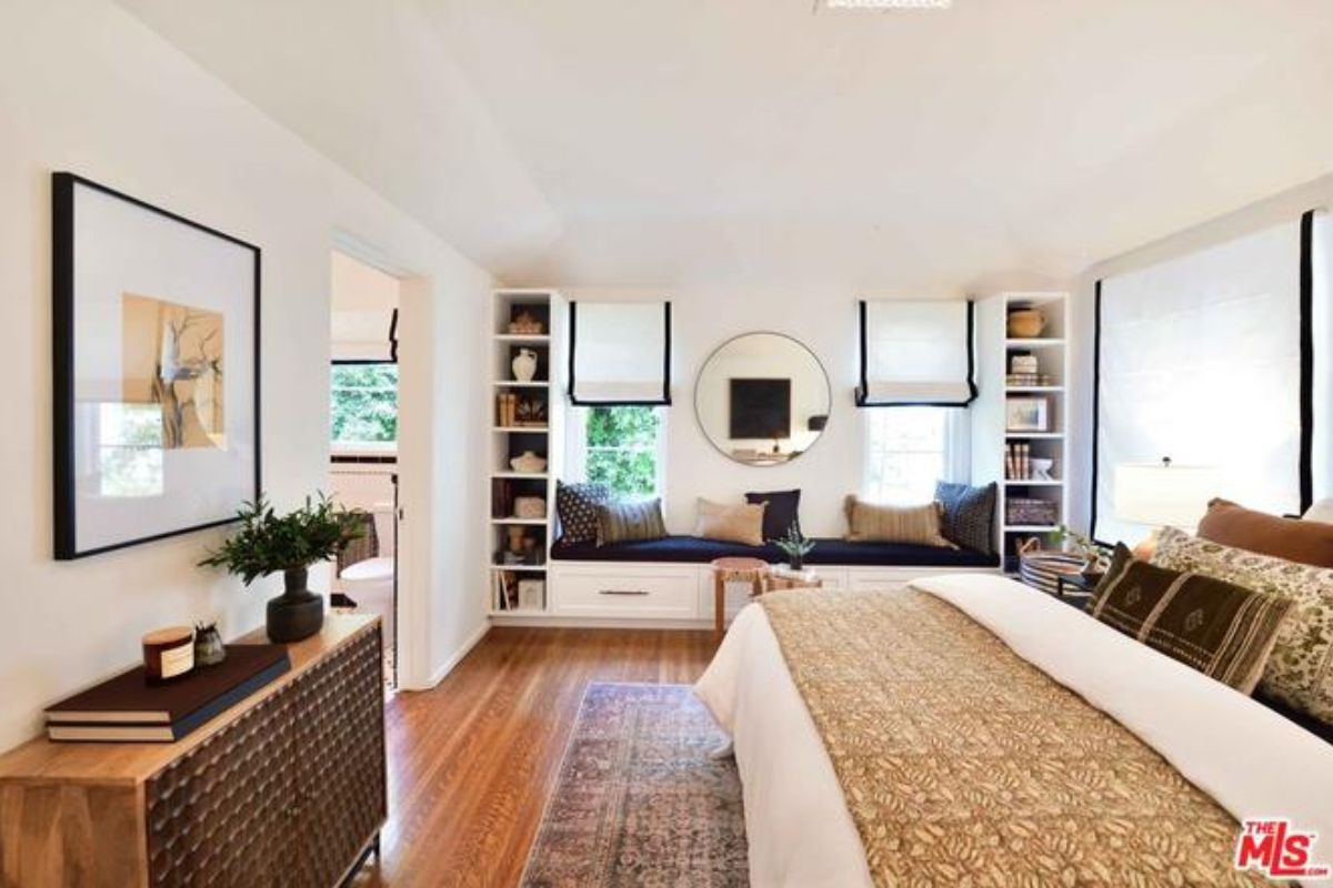 A bedroom with a bed, cabinet, shelves, window, and window seating.