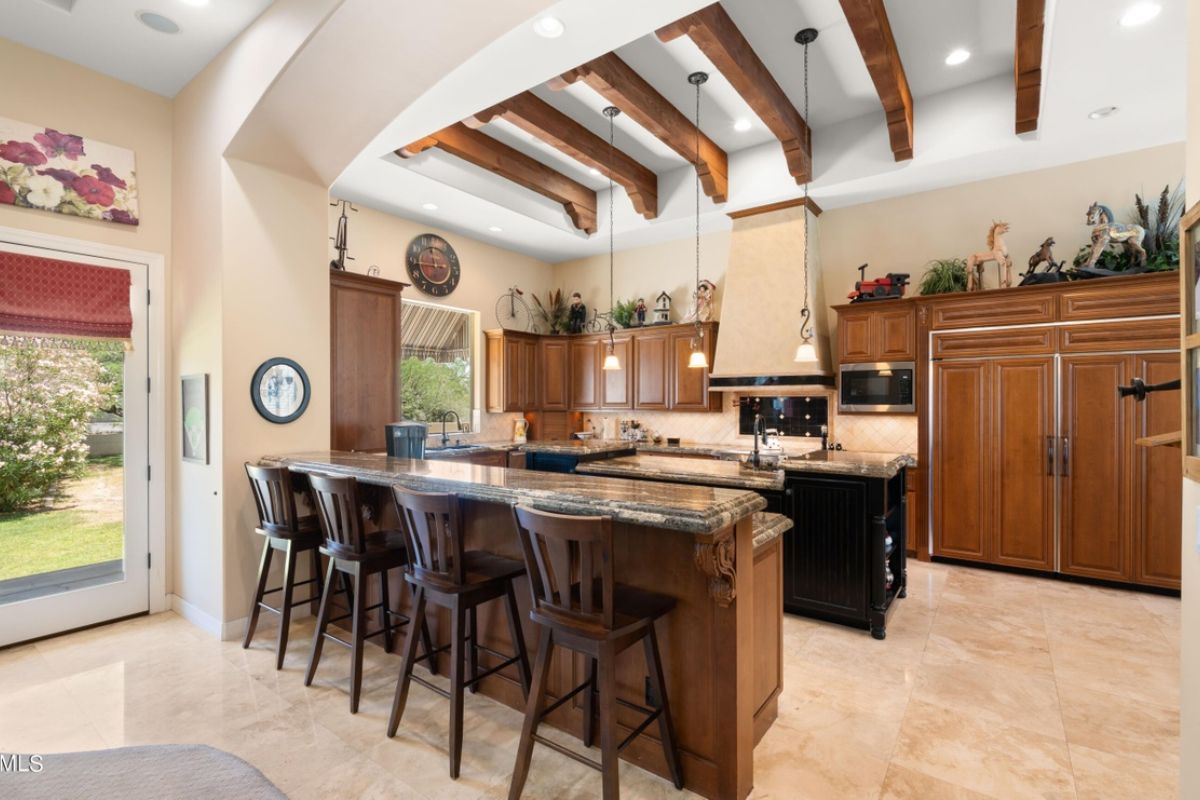 A kitchen with an exposed beam ceiling, countertops, stools, and cabinets.