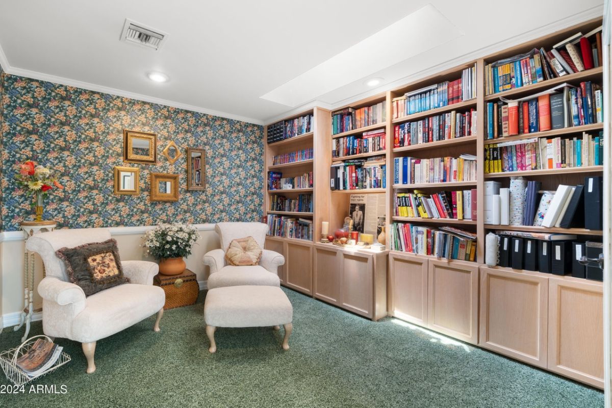 A reading nook with bookshelves, cabinets, wallpaper, and chairs.