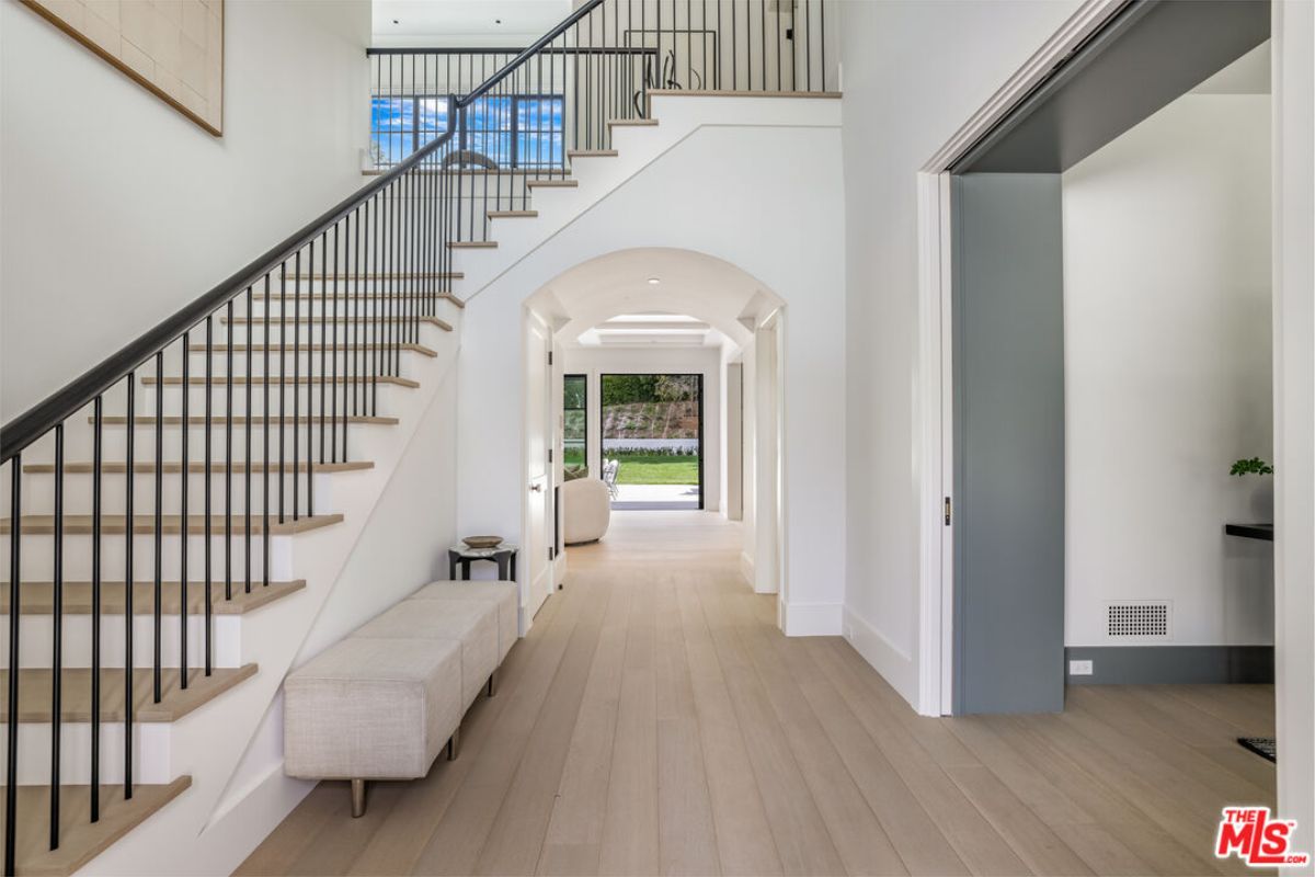 A foyer with wooden floors, a bench, and a staircase.