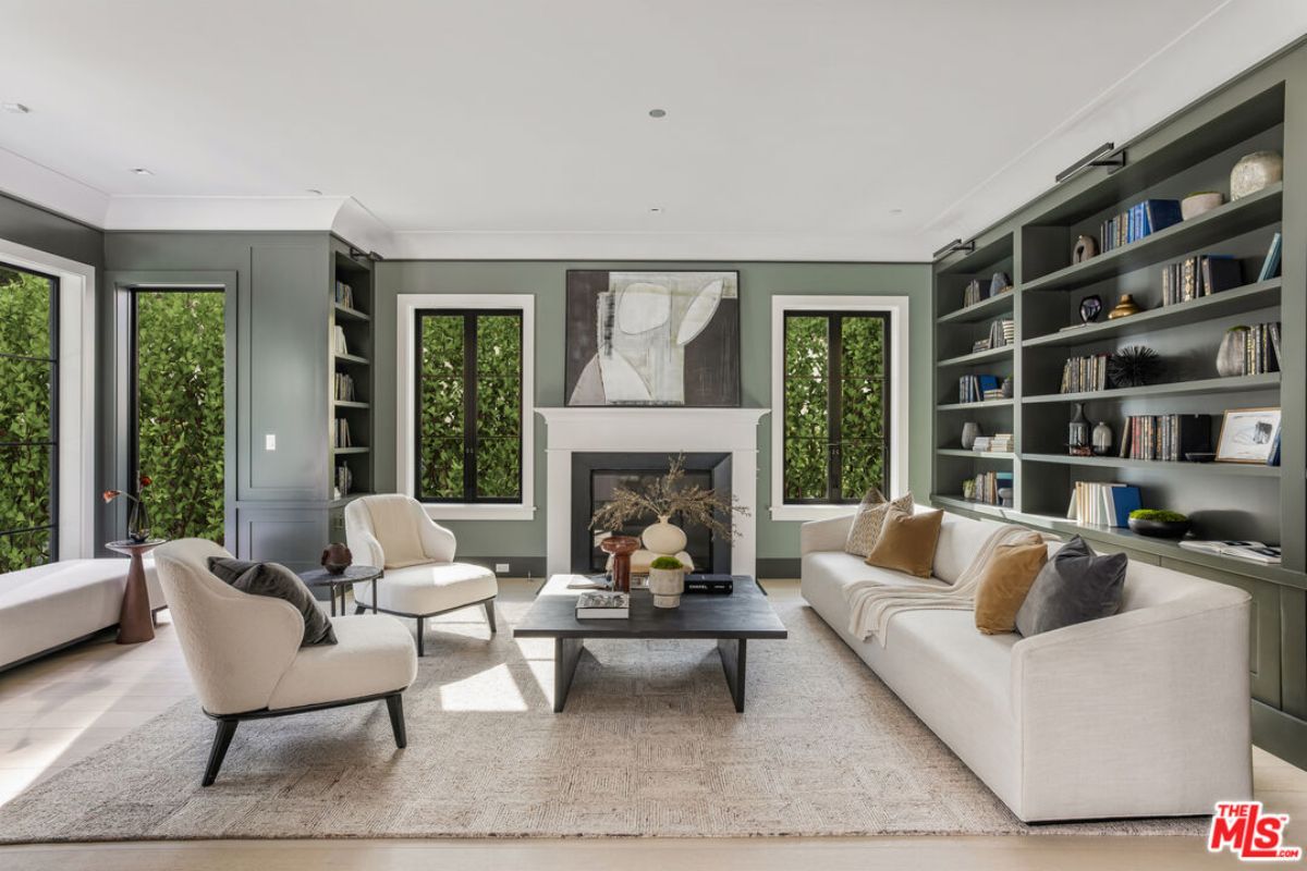 A living room with windows, fireplace, shelves, couch, chairs, and a center table.