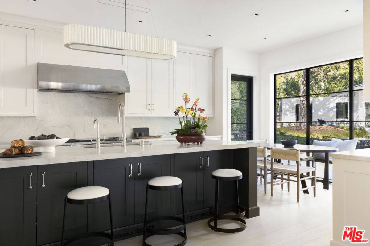 A kitchen with countertops, stools, sink, cabinets, and a dining table with chairs.