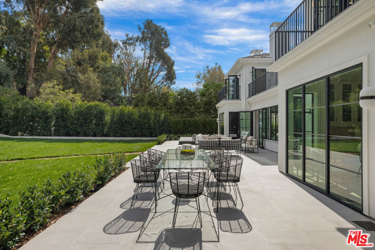 A patio with a glass dining table surrounded by chairs.