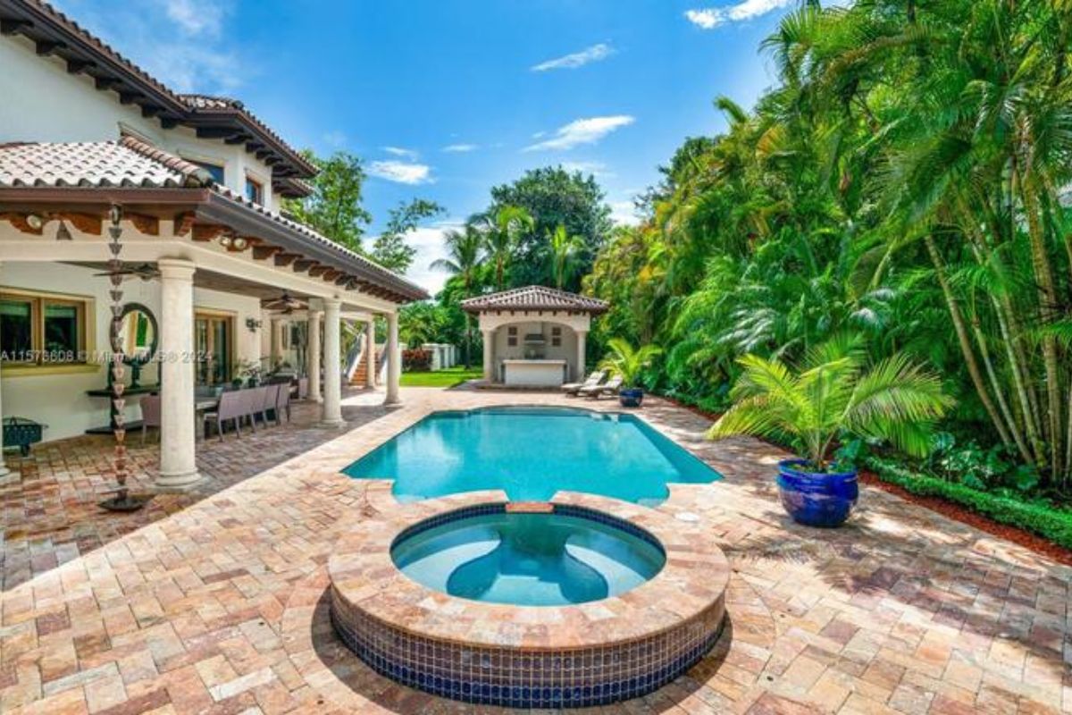 A swimming pool with a jacuzzi surrounded by plants and trees on the poolside.