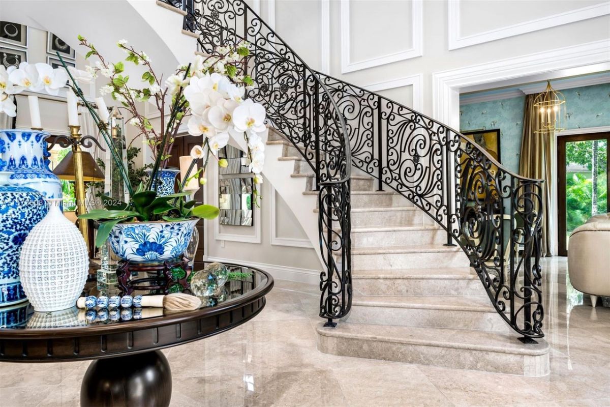 A foyer with a tiled floor, a round table adorned with vases, and a staircase.