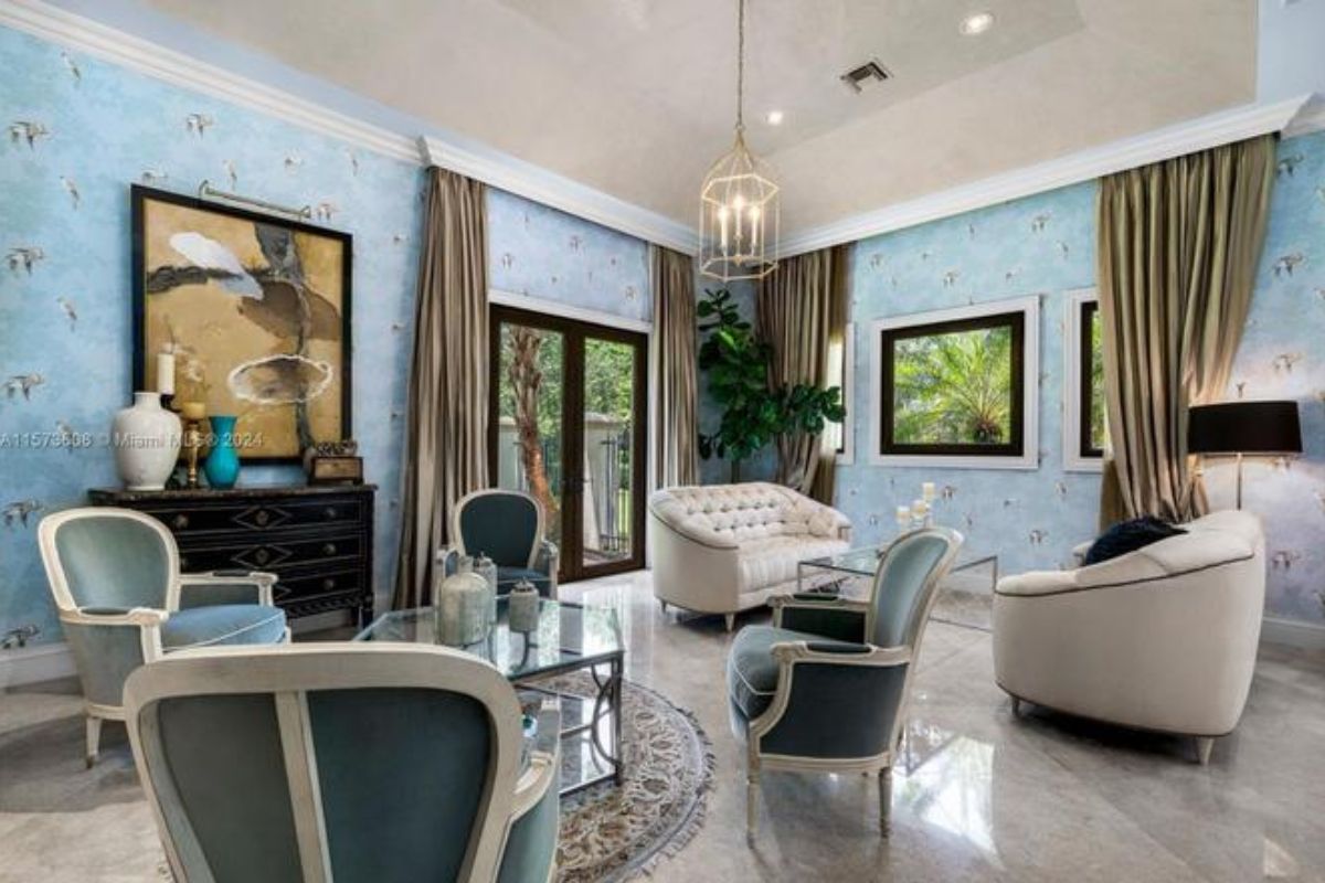 A living room with wallpaper, tiled floor, cabinets, couches, chairs, and coffee tables.