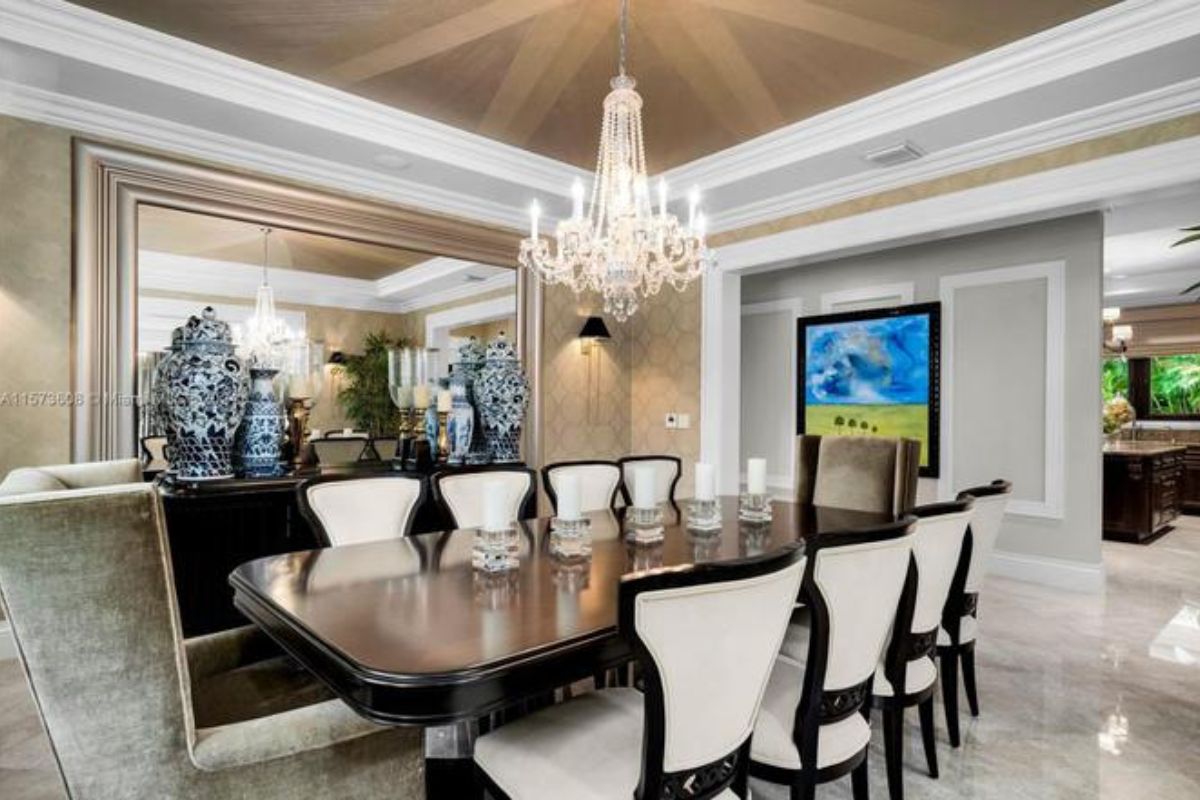 A dining room with a painting, mirror, vases, chandelier, and a dining table surrounded by chairs.